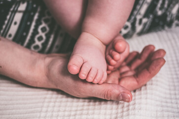 The little naked leg of the baby is carefully placed in the warm hand of the mother