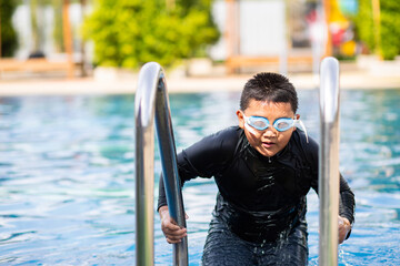 Fat asian boy in swimsuit and goggles swimming in the pool