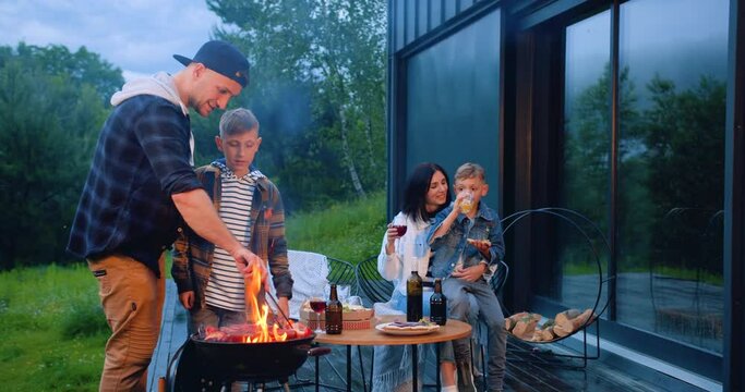 Family leisure concept where good-natured adorable happy parents and children cooking bbq party outdoors near own house