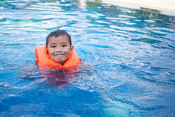 Fototapeta na wymiar Asian boy in swimsuit and life jacket swimming in the pool