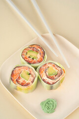 Fresh sushi roll with cucumber, salmon and avocado with chopsticks on a beige background. Healthy food Japanese cuisine. Modern style, top view