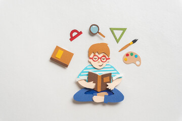Boy in glasses  reading educational textbook. Education supplies around schoolchild. Illustration from paper
