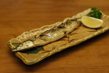 Fototapeta na wymiar close up salt baked saury with lemon on plate on wooden table. Traditional Japanese cuisine