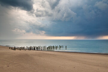 Stormy clouds over the Baltic sea. Abandoned and collapsed wooden pier on the sandy shore.  