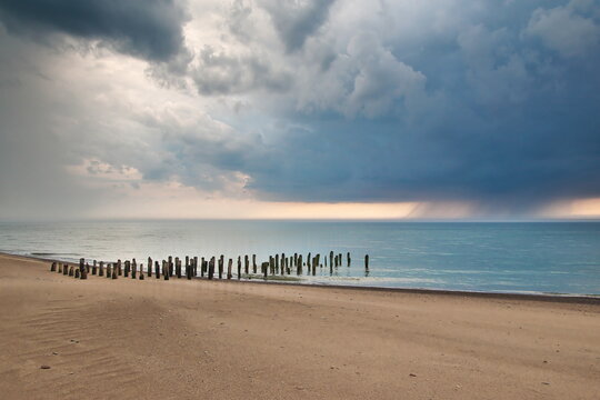 Stormy clouds over the Baltic sea. Abandoned and collapsed wooden pier on the sandy shore.  
