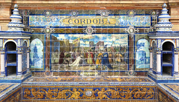 Image with the name of the spanish city of Cordoba and a historical scene painted on ceramic tiles - seating benches in Spain Square in Seville