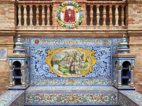 Image with the name of the spanish city of Cuenca and a historical scene painted on ceramic tiles and the emblem shield - seating benches in Spain Square in Seville
