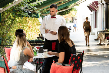 A young waiter serves a drink in the garden of the cafe restaurant