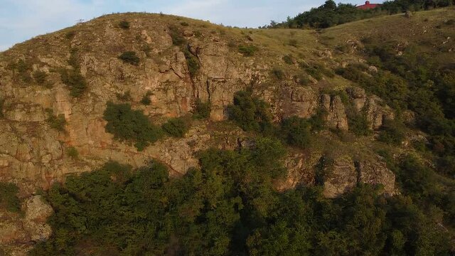 aerial photography drone shot of a mountain river, flying backwards over a mountain, passing by green river banks in the sunset, small rocks with rapids, sunlight on the water surface