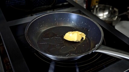 Piece of butter on pan with oil. Close up of black pan on hotplate in the restaurant, preparing for frying food at the kitchen restaurant