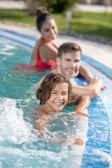 Fototapeta na wymiar Joyful boy and parents in water of outdoor pool
