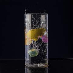 A slice of lemon falls into a glass of water on a black background.