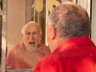 Un homme âgé s'amuse à faire des grimaces devant un miroir. Il tire la langue.