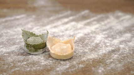 Two raw italian green, white tortellini on wooden table, italian flag colors. Close up of raw italian tortellini with flour on restaurant kitchen table