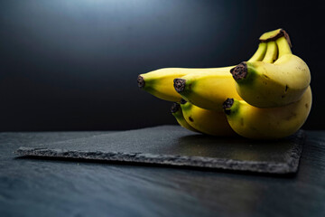 Close-up of a bunch of yellow bananas on a serving black board against a dark background. Free copy space. School snacks or organic food concept