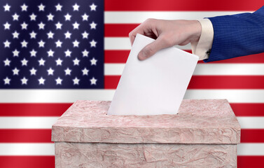 Man throws ballots into the ballot box against the background of the American flag.