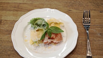 Tortellini on white plate with fork on wooden table, with parmesan. Close up tortellini of different colors, green, white, red on white plate with melting butter