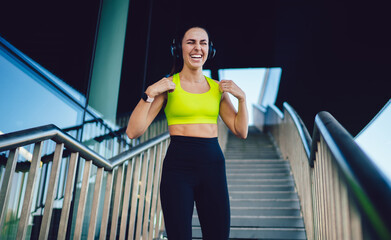 Excited Caucasian woman jogger in bluetooth headphones for noise cancellation enjoying active...