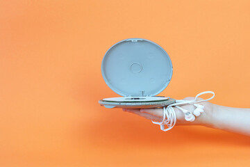 A female hand holds a portable MP-player with white headphones on an orange background. Copy space...