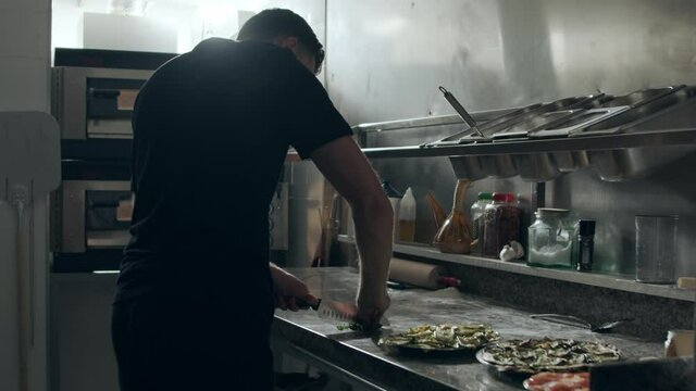Pizza maker cutting parsley in kitchen