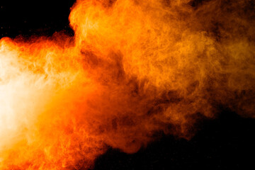 Abstract orange powder explosion. Closeup of orange dust particle splash isolated on black...