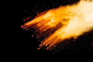 Abstract orange powder explosion. Closeup of orange dust particle splash isolated on black background.