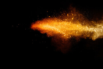 Abstract orange powder explosion. Closeup of orange dust particle splash isolated on black background.