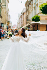 Naklejka premium Happy bride with a long veil posing on the streets of the city.