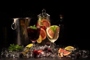 Two glasses of white and red wine sangria with blackberries, strawberries, grapefruit, lime and orange slices with ice and mint