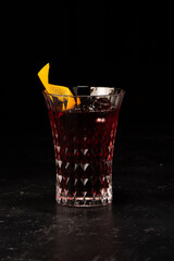Alcoholic cocktail with berry syrup and orange peel decoration in a small faceted glass