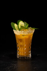 Alcoholic cocktail with orange juice, ice and cucumber and sesame decoration in a small faceted glass