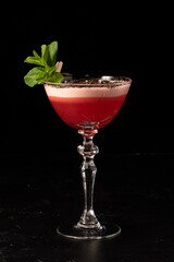 Beautiful red alcoholic cocktail with milk foam and coffee beans, decorated with mint leaves in a transparent glass on a dark background