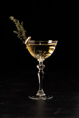 Beautiful alcoholic cocktail decorated with thyme in a transparent glass on a dark background