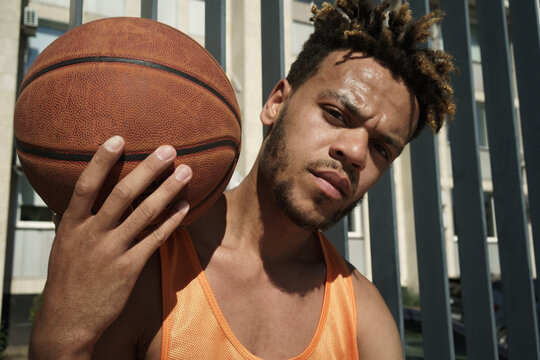 Image of african american guy posing with basketball on sports ground