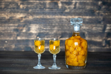 Homemade tincture of yellow cherry plum in a crystal bottle and a two wine crystal glass on wooden background, Ukraine