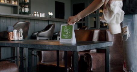 Female waiter placing sanitized table sign on a table in a restaurant, COVID-19 pandemic, coronavirus spread preventive measures