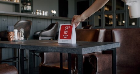 Fototapeta premium Waitress placing warning sanitizing sign on a table in a restaurant, COVID-19 pandemic, coronavirus spread preventive measures