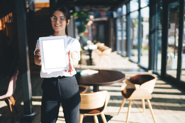 Half length portrait of cheerful prosperous woman owner of cafeteria enjoying career showing digital tablet with blank screen,prosperous brunette female holding touchpad with mock up monitor