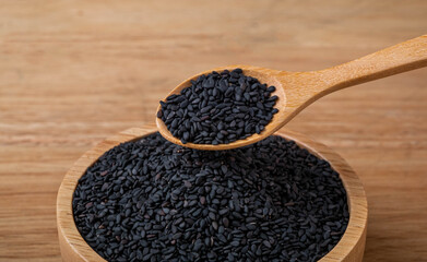 Black sesame seeds in a wooden spoon and bowl focus on the spoon on the table,, organic  food concept.