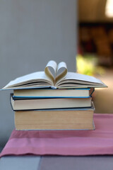 Stack of hardcover books on a table. Top books has pages folded in a heart shape. Selective focus.