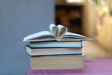 Stack of hardcover books on a table. Top books has pages folded in a heart shape. Selective focus.