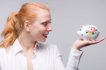 Fototapeta na wymiar Young red haired woman looking happy at her piggy bank / porcelain bank