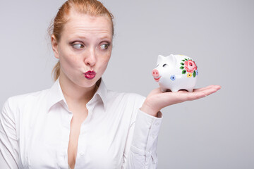 Fototapeta na wymiar Young red haired woman with kiss mouth holding a piggy bank / porcelain bank