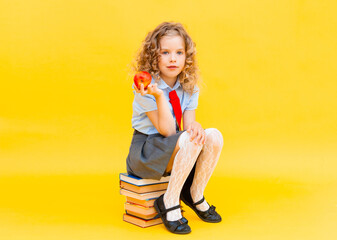 schoolgirl in a school uniform holding a stack of books and a red apple on a yellow background. Concept of learning and school.