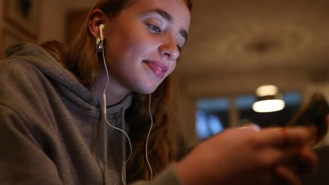 junge Frau mit Kopfh&ouml;rer im Ohr h&ouml;rt Musik mit ihrem Smartphone