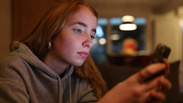 junge Frau schreibt abends mit ihrem Smartphone, das Gesicht wird dabei vom Display angeleuchtet
