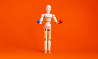Wooden figure of a mannequin holding a red pill and blue pill on a orange background. Coronavirus, pandemic and epidemic concept. Matrix imitation.