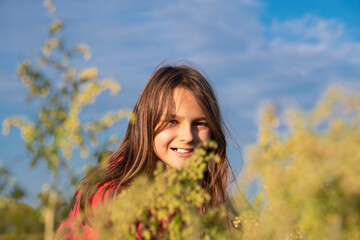 Naklejka na ściany i meble A girl with a missing tooth smiles in the tall grass in a field in summer