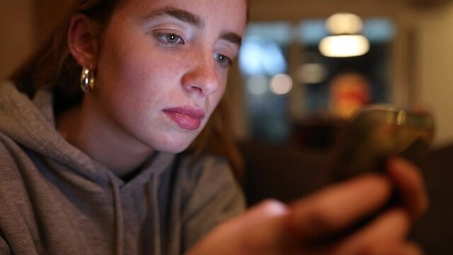 junge Frau schreibt abends mit ihrem Smartphone, das Gesicht wird dabei vom Display angeleuchtet