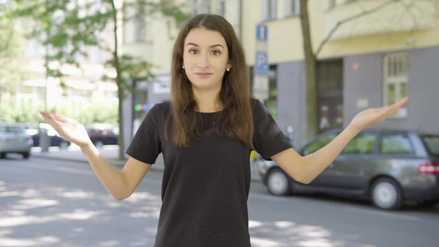 A young Turkish woman acts frustrated and at a loss as she looks at the camera in the street in an urban area  - a road with cars and a building in the blurry background